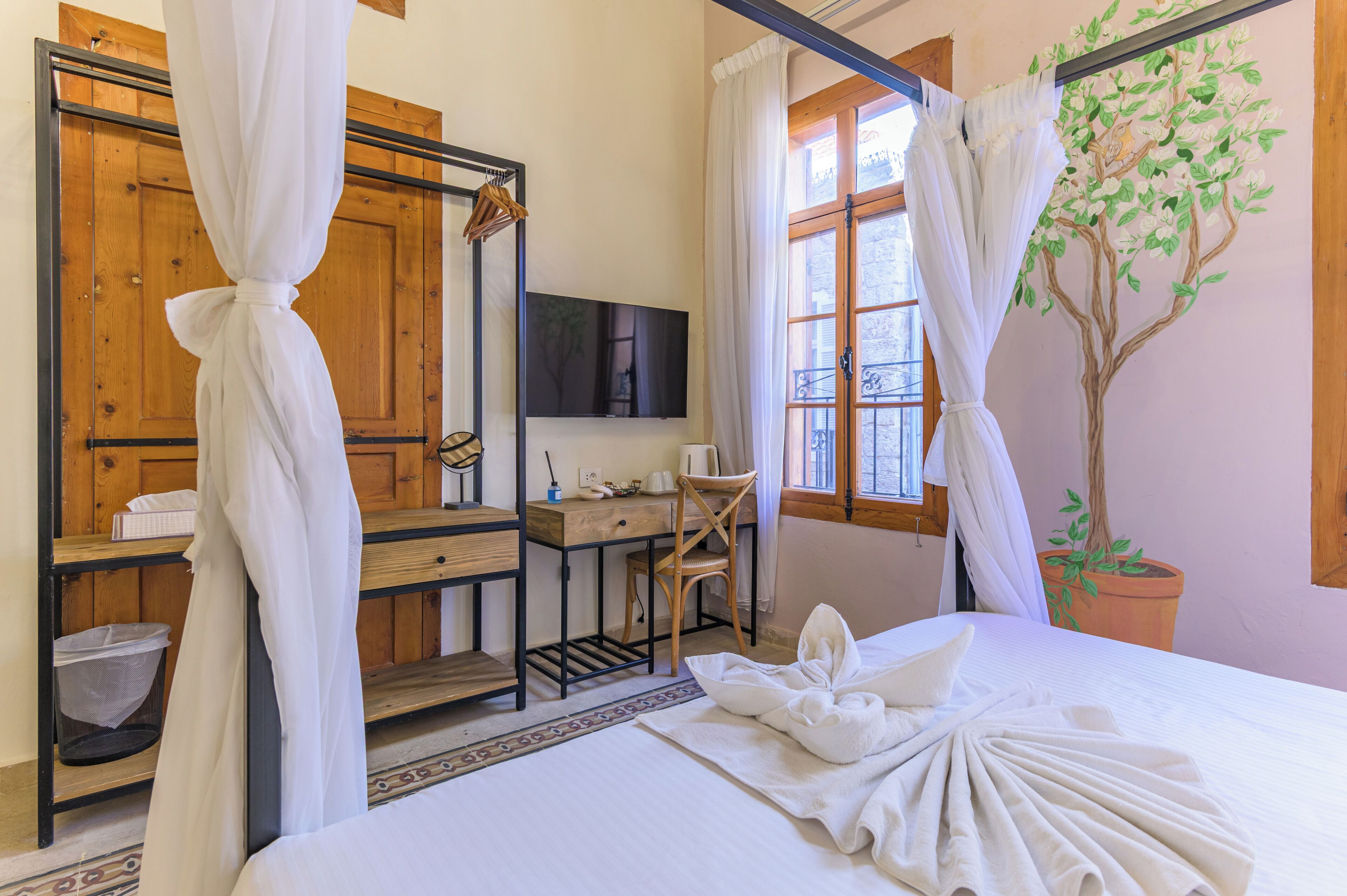 Quarto com cama, escrivaninha, cadeira, televisão, planta em vaso e janela com cortinas.