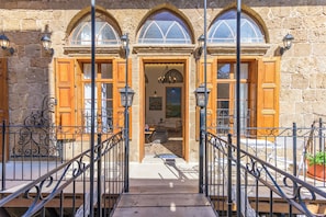 Un bâtiment en pierre avec des portes et des fenêtres en bois, un escalier et du mobilier d’extérieur.