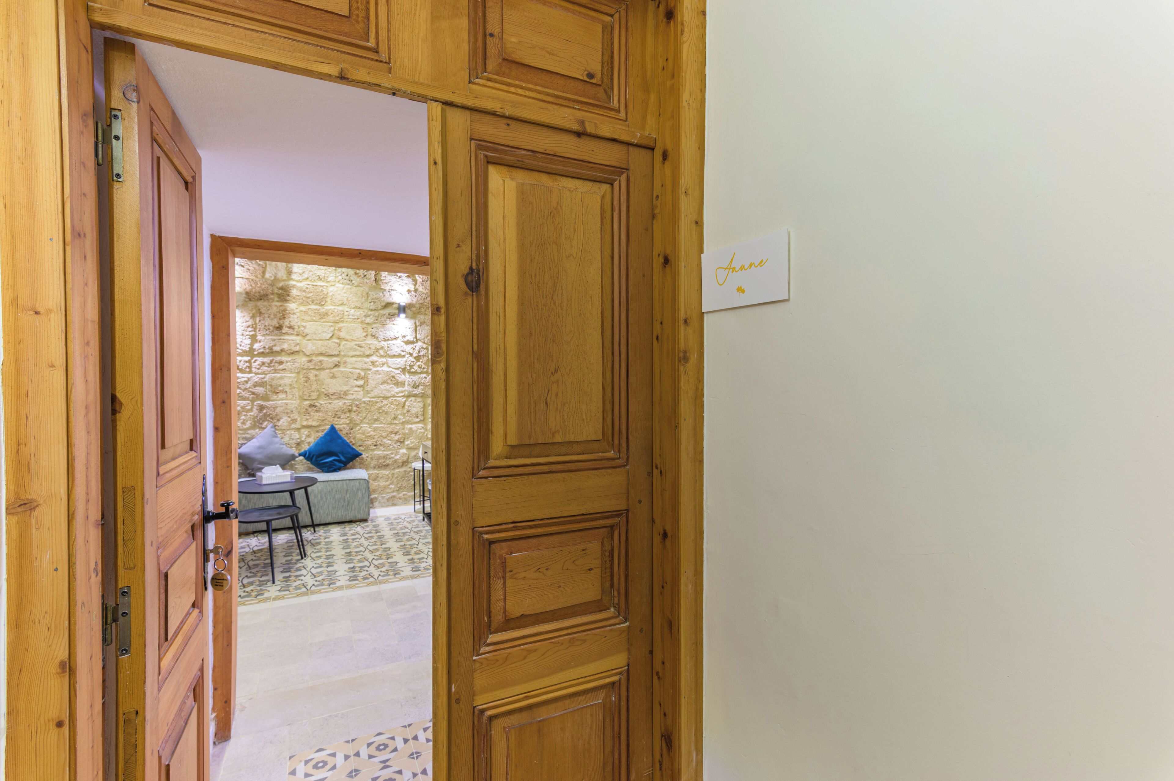 A wooden door leading to a room with a stone wall, a small table, and a blue pillow.