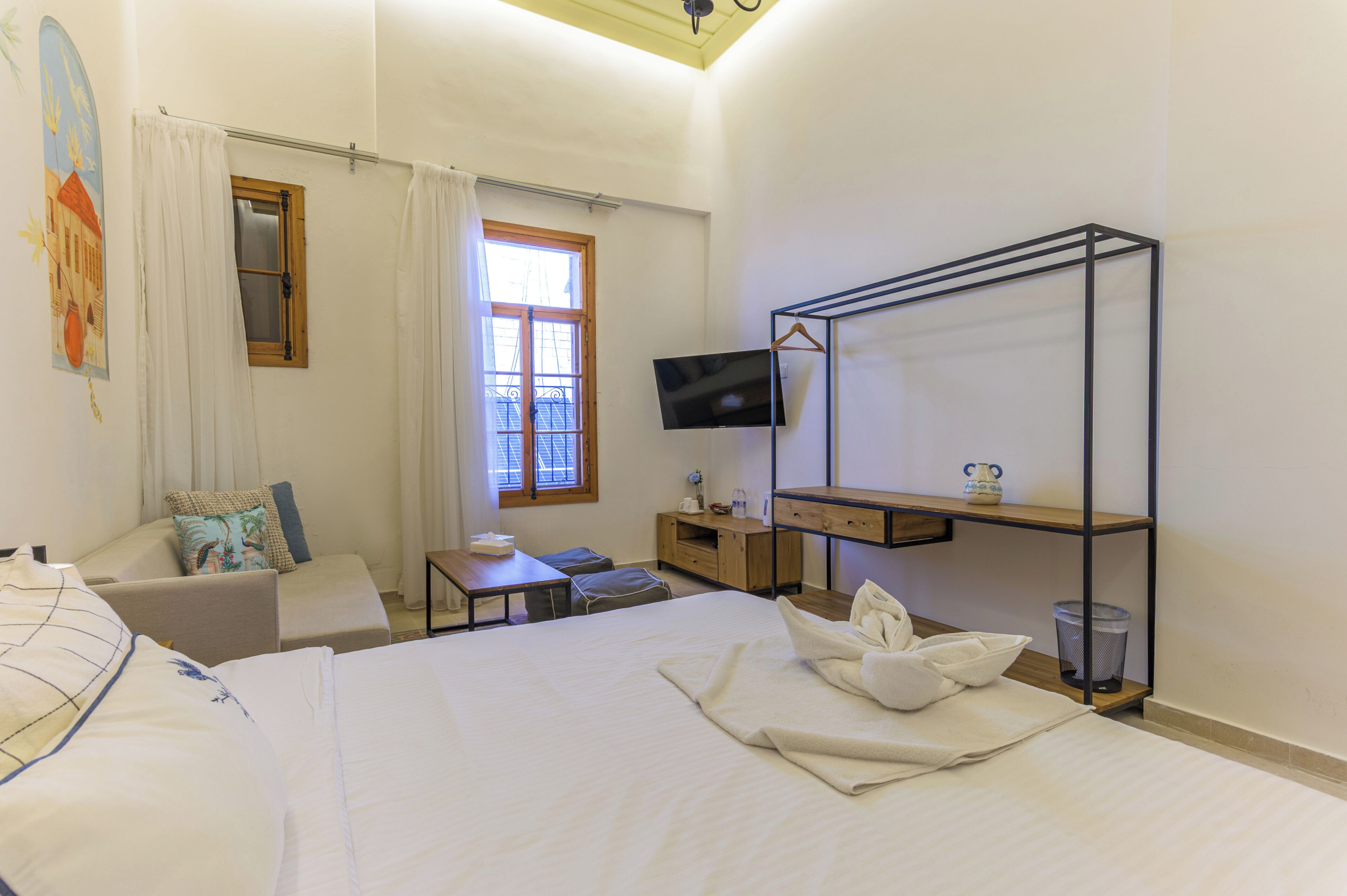 Una camera d'albergo con un letto, una scrivania, una televisione, una finestra con tende e uno scaffale a parete.