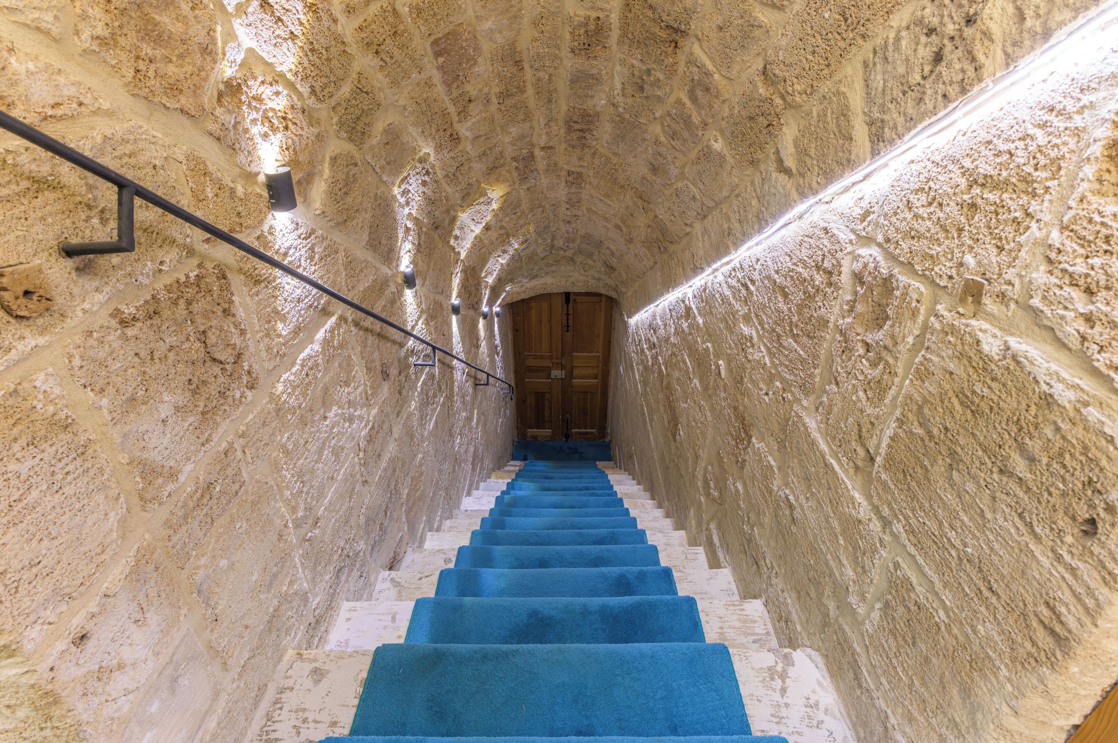 Un escalier en pierre recouvert d’une moquette bleue mène à une porte en bois située en haut.