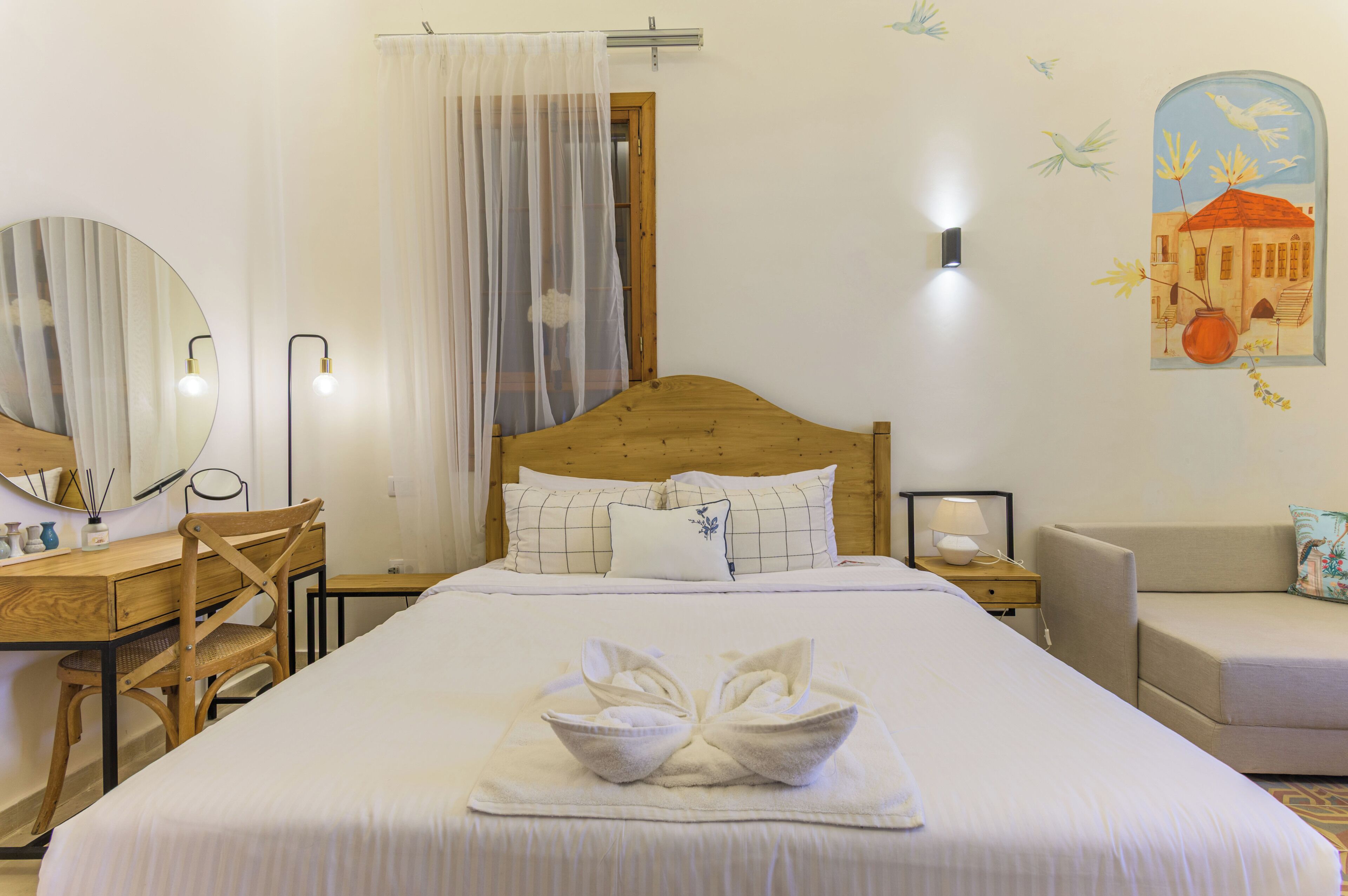 Una camera d'albergo con un letto in legno, una scrivania con una sedia, un comodino con una lampada e uno specchio fissato alla parete.