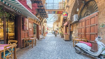 Une rue pavée avec un scooter garé, des tables et des chaises en bois, et un bâtiment avec une enseigne.