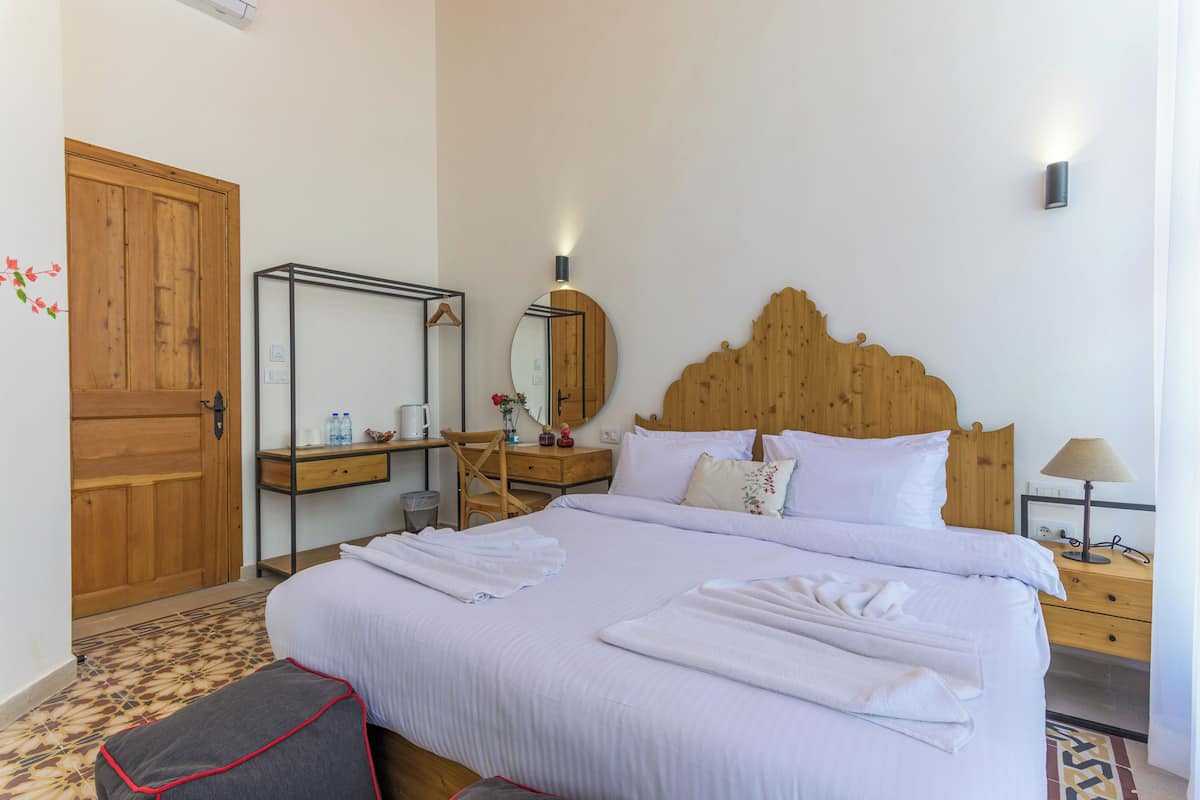Una habitación de hotel con una cama grande, cabecera de madera, mesitas de noche, un espejo y un armario.