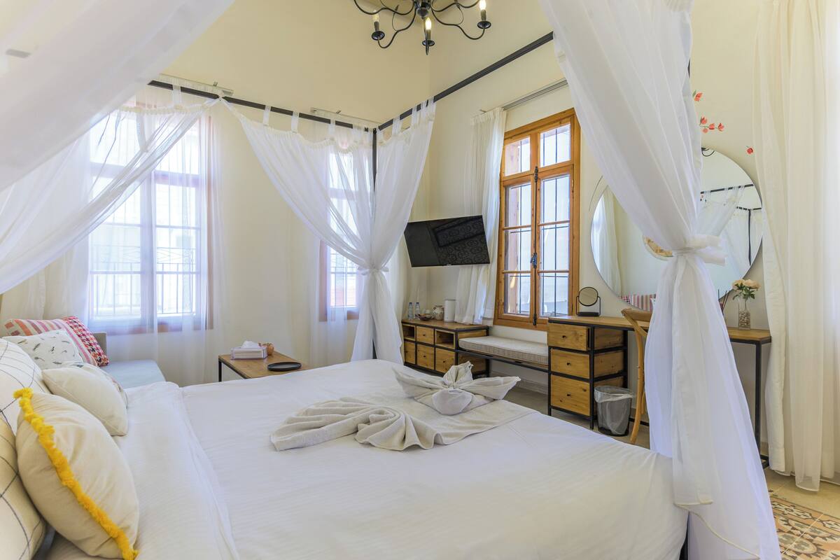 Un dormitorio con cama, escritorio, televisor y ventana con cortinas.