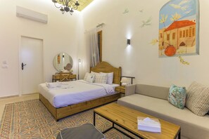A bedroom with a bed, a sofa, a coffee table, a mirror, and a wall with a painting. - Les Bougainvilliers Studios in Batroun (Batroun)