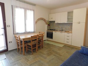 A compact kitchen with a dining table and chairs, a stove, and cabinets. - Lovely apartment with garden in the Gulf of Orosei 5 minutes from the sea (Orosei)