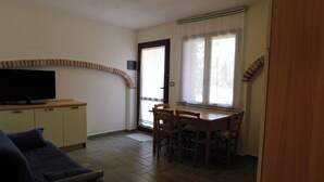 Un salon équipé d’un téléviseur, d’un canapé, d’un coin repas avec une table et des chaises, et d’une cuisine avec des placards.