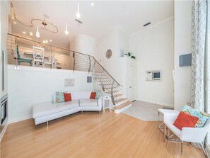 En rummelig opholdsstue med en hvid sofa, en hvid lænestol, en trappe og en balkon med gelænder.