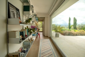 A modern interior with a bookshelf, a patterned rug, and a view of the outdoors. - Nestled among the gentle hills of San Marcello, where the eye wanders across lush greenery and the silhouette of the mountains, stands a private villa designed for those who wish to slow down, breathe deeply, and enjoy the luxury of time.Offering 500 sqm (San Marcello)