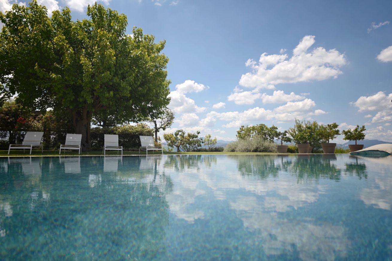 A clear swimming pool with lounge chairs and trees in the background.