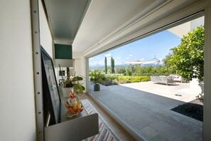 A modern room with a large window, a potted plant, and a small table with decorative items. - Nestled among the gentle hills of San Marcello, where the eye wanders across lush greenery and the silhouette of the mountains, stands a private villa designed for those who wish to slow down, breathe deeply, and enjoy the luxury of time.Offering 500 sqm (San Marcello)