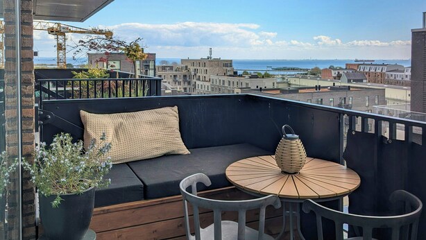 Een balkon met een bank, een ronde tafel en een bloempot.