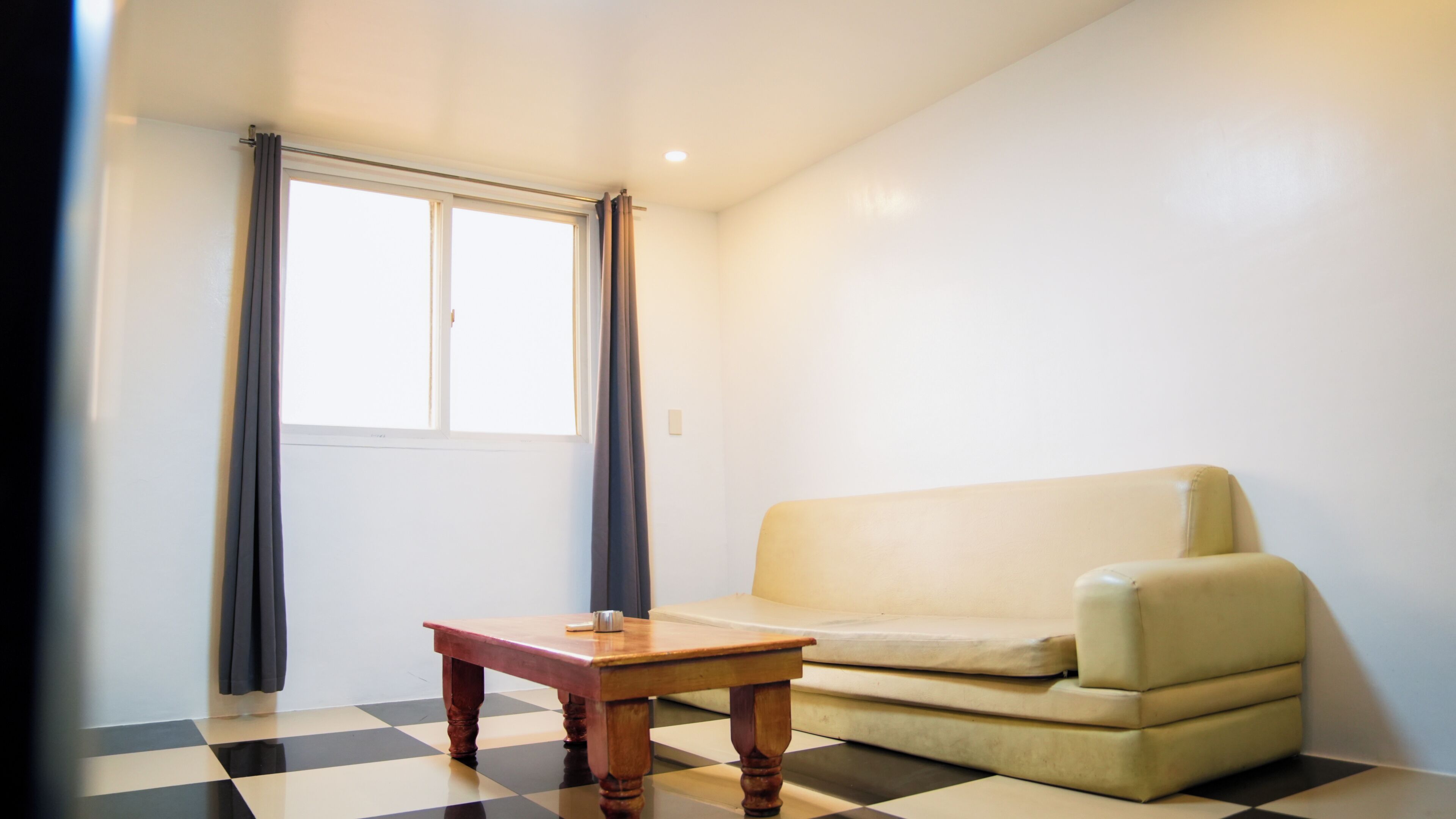 A room with a checkered floor, a sofa, a wooden table, and a window with curtains.