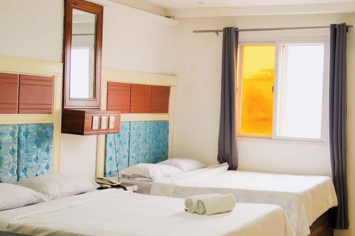 Hotellihuone, jossa on kaksi sänkyä, työpöytä, peili ja ikkuna, jossa on verhot.