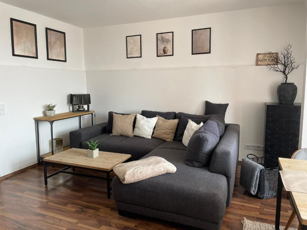 Ein modernes Wohnzimmer mit einem Ecksofa, einem Couchtisch, einem Beistelltisch mit Lampe und einer dekorativen Vase.