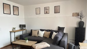 Ein modernes Wohnzimmer mit einem Ecksofa, einem Couchtisch, einem Beistelltisch mit Lampe und einer dekorativen Vase.
