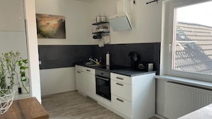Eine kompakte Küche mit weißen Schränken, einer schwarzen Arbeitsplatte, einem eingebauten Backofen und einem Fenster mit Blick.