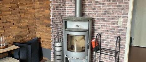 A wood-burning stove in a corner with a brick wall, a wooden bench, and a metal rack.