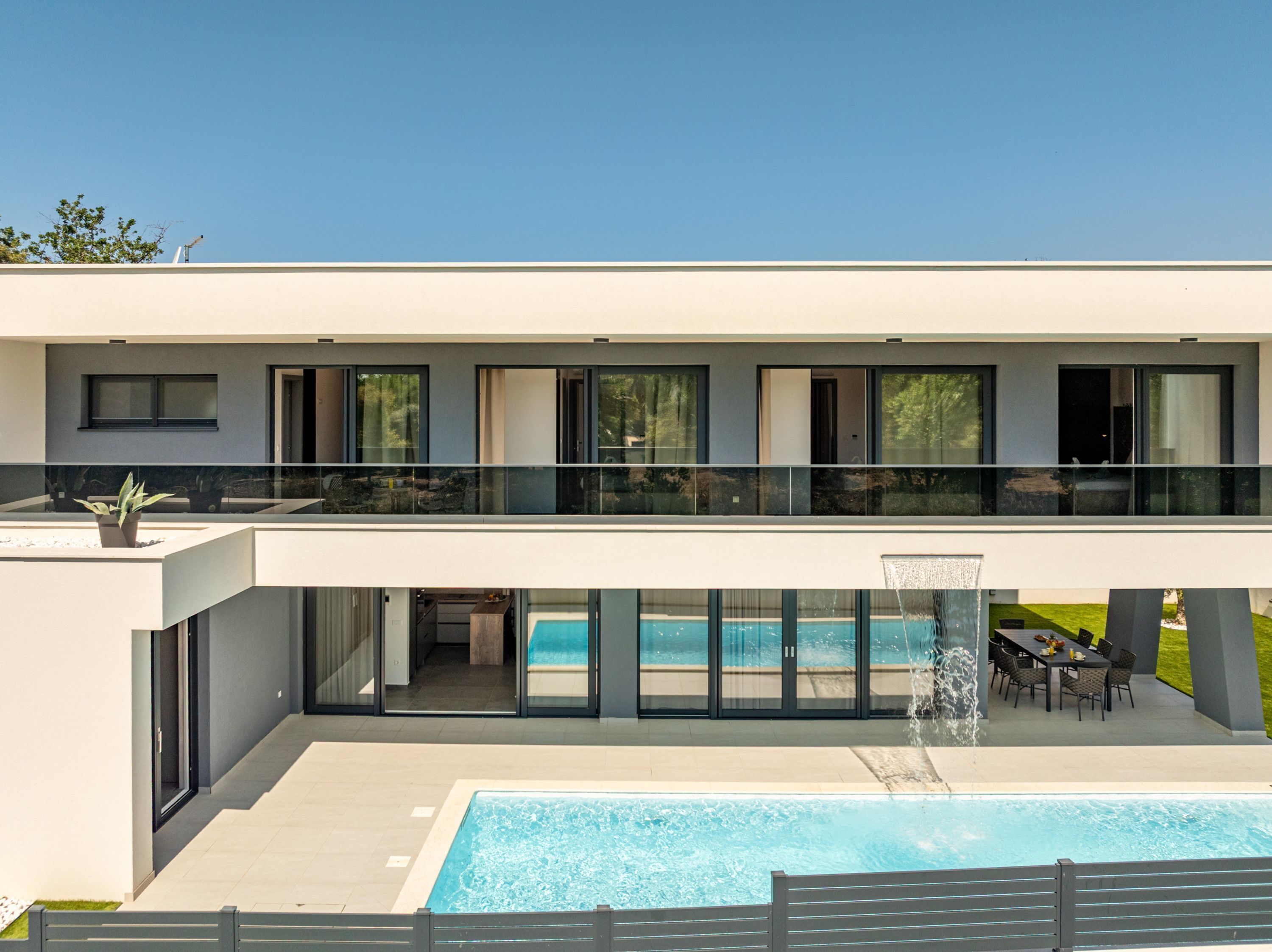 A modern two-story house with a swimming pool, outdoor seating, and a glass balustrade.