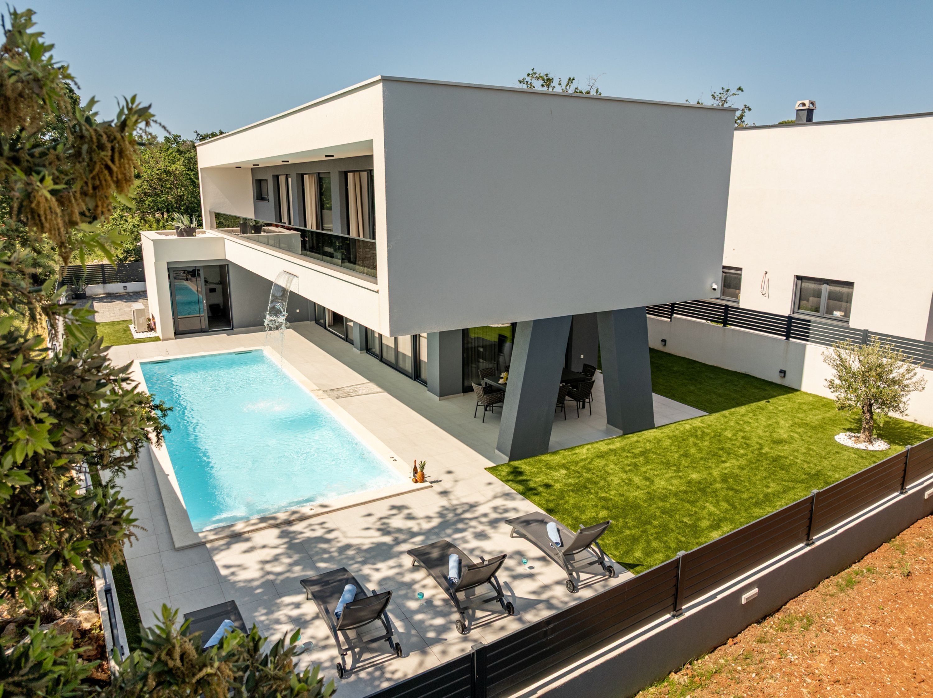 A modern two-story house with a swimming pool, outdoor seating, and a well-maintained lawn.
