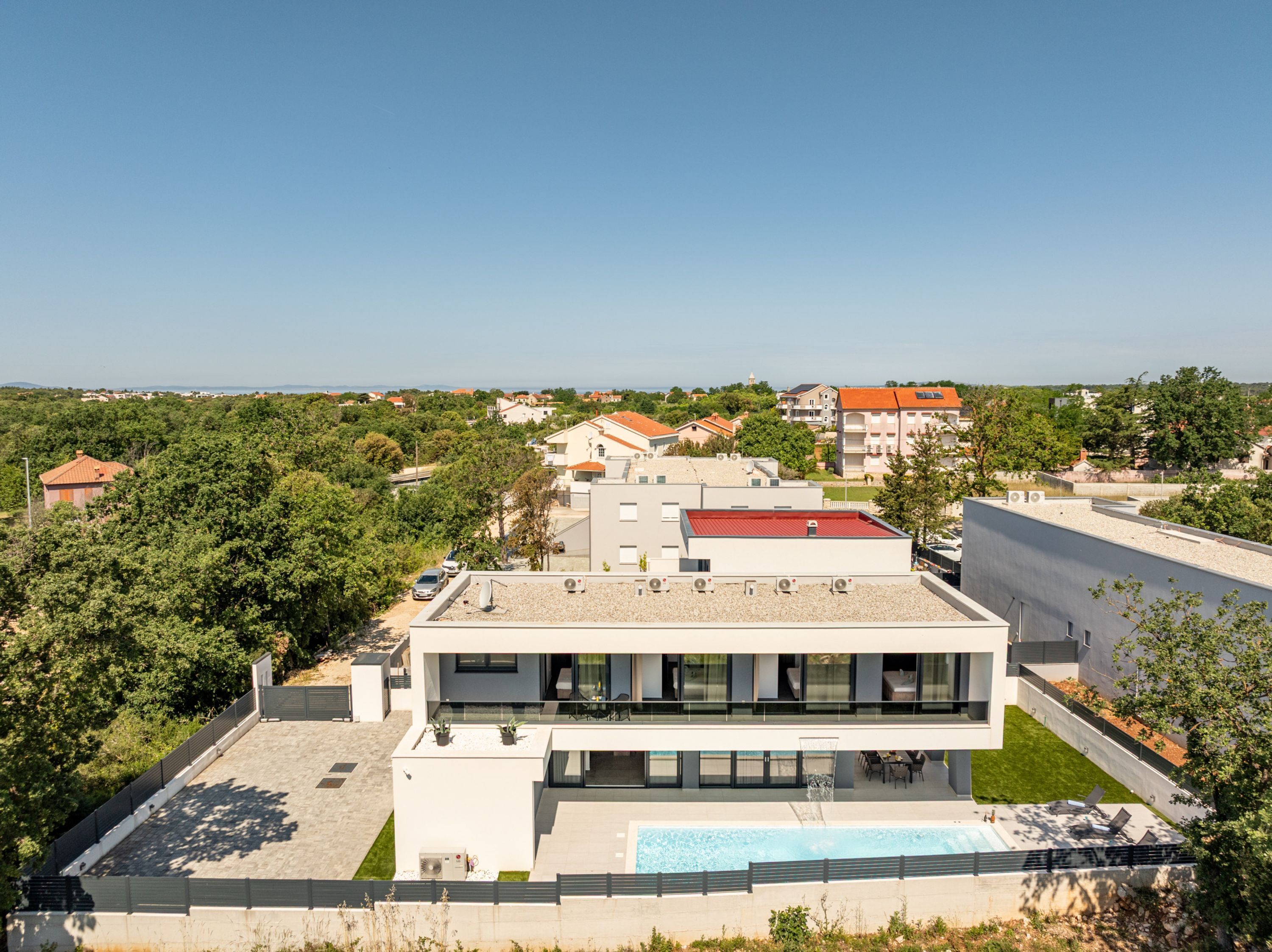 Un edificio moderno con piscina en la azotea, rodeado de vegetación y otros edificios residenciales.