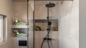 Una ducha moderna con cabezal de ducha manual, panel de control y repisa con artículos de aseo.
