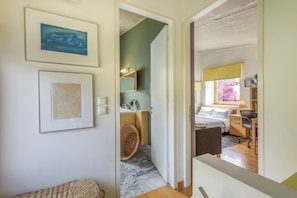 Ein Flur, der in ein Schlafzimmer mit Bett, Nachttisch und Fenster mit Aussicht führt.