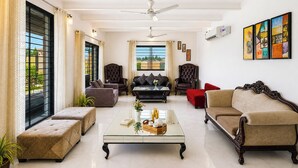 A spacious living room with a glass coffee table, leather sofas, and a view through large windows. - Alaya Stays Batlaw Classic 5 BHK Villa with Pvt Pool & Gazebo (Gurugram)
