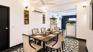 A dining area with a table set for six, chairs, a ceiling fan, wall-mounted lights, and a decorative plant. - Alaya Stays Batlaw Classic 5 BHK Villa with Pvt Pool & Gazebo (Gurugram)