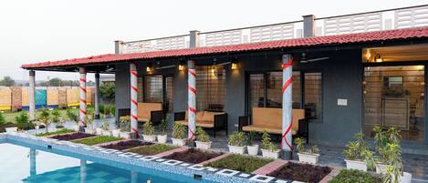 A hotel with a swimming pool, outdoor seating, and potted plants.