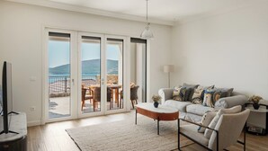 A living room with a sofa, coffee table, and a view through glass doors to an outdoor patio. - Sea View Apartment in Luštica Bay (Radovići)
