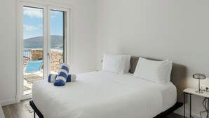 A hotel room with a large bed, a view of the sea, and a stone wall. - Sea View Apartment in Luštica Bay (Radovići)