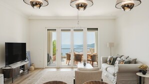 A living room with a TV, sofa, and dining area with a view. - Sea View Apartment in Luštica Bay (Radovići)