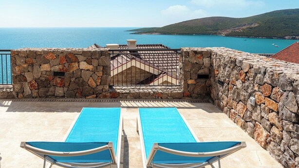 A rooftop pool with two lounge chairs, stone walls, and a view of the sea and hills. - Sea View Apartment in Luštica Bay (Radovići)
