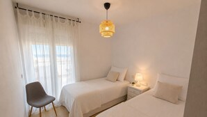 Camera da letto con due letti, una sedia, un comodino con una lampada e un lampadario.
