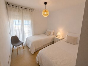 Ein Schlafzimmer mit zwei Betten, einem Sessel, einem Nachttisch mit Lampe und einer Pendelleuchte.
