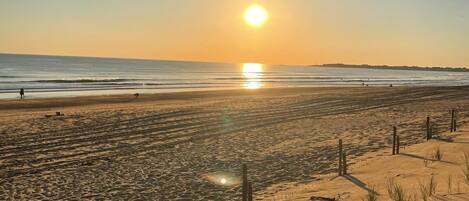A beach with a fence, sand dunes, and a sunset.