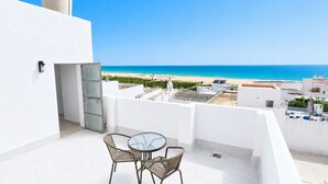 A balcony with a glass table and wicker chairs, overlooking a beach and ocean. - CREA Conil Apartments II (Conil de la Frontera)