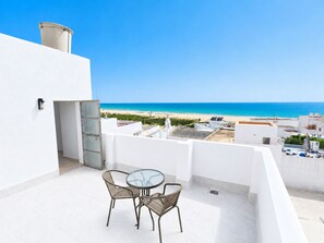 Ein Balkon mit Glastisch und Korbstühlen mit Blick auf einen Strand und den Ozean.