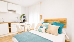 A modern hotel room with a bed, a small desk, a microwave, a sink, and a window with curtains. - CREA Conil Apartments II (Conil de la Frontera)