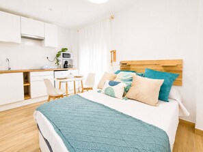 Ein modernes Hotelzimmer mit einem Bett, einem kleinen Schreibtisch, einer Mikrowelle, einem Waschbecken und einem Fenster mit Vorhängen.