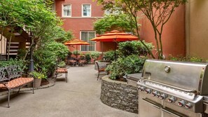 Un patio al aire libre con una parrilla, mesas, sillas y sombrillas.