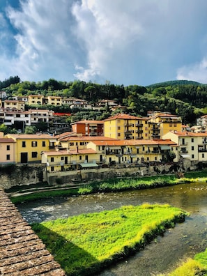 A riverside town with buildings along the water, a bridge, and a hillside in the background.