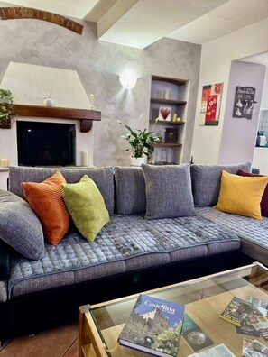 A living room with a grey sofa, a fireplace, a bookshelf, and a glass coffee table with a book.