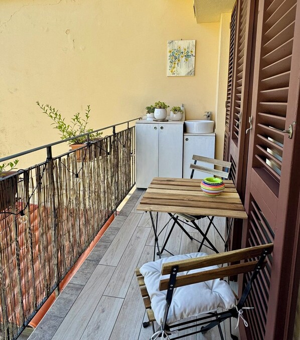 A balcony with a wooden table, a bench, potted plants, and a small cabinet with a sink.