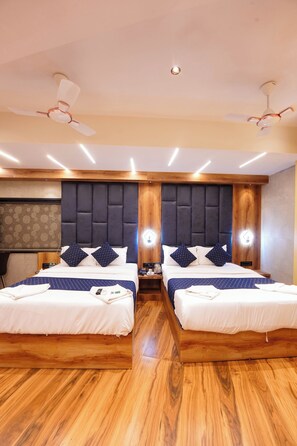 A hotel room with two beds, wooden flooring, a dark headboard, and ceiling fans.