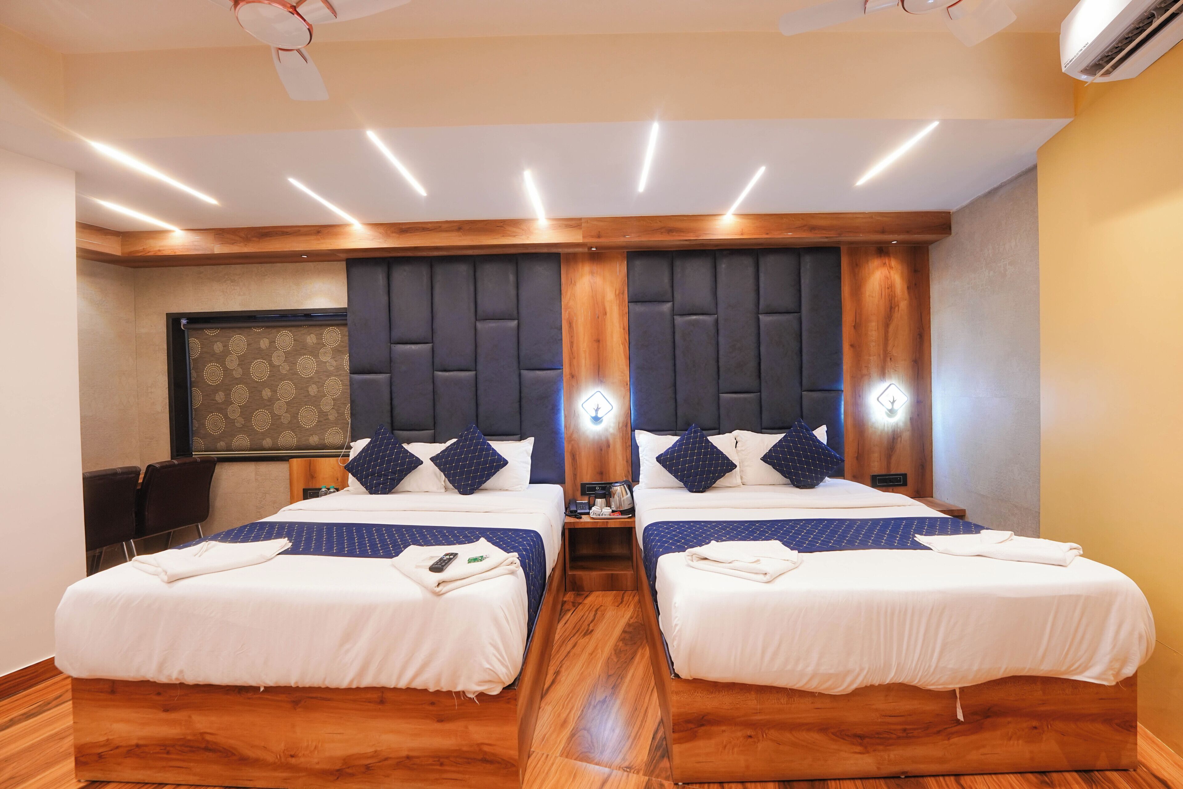 Ein Hotelzimmer mit zwei Betten, Holzboden, einem dunklen Kopfteil und einem an der Wand montierten Fernseher.