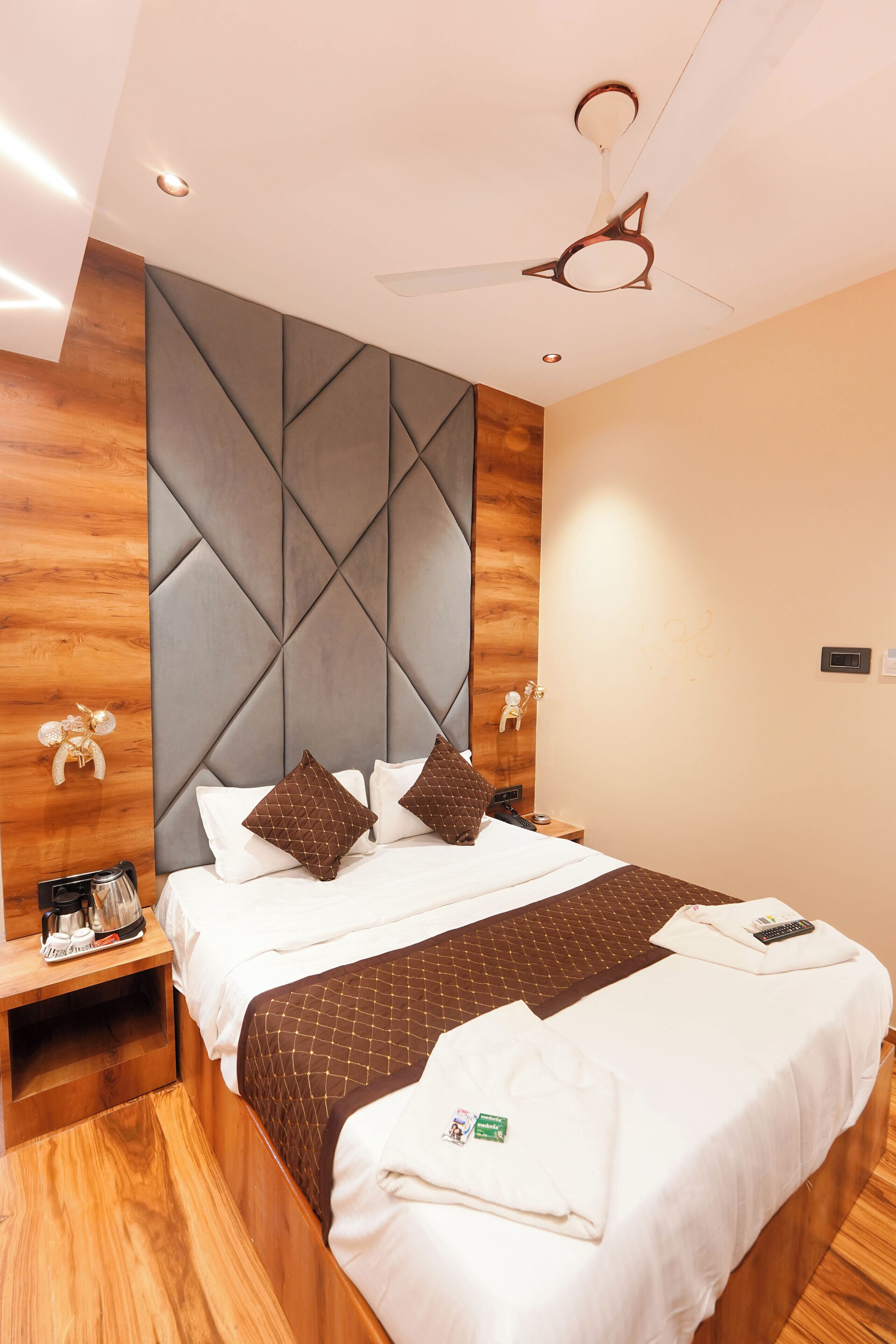 A modern hotel room with a large bed, wooden headboard, and a ceiling fan.