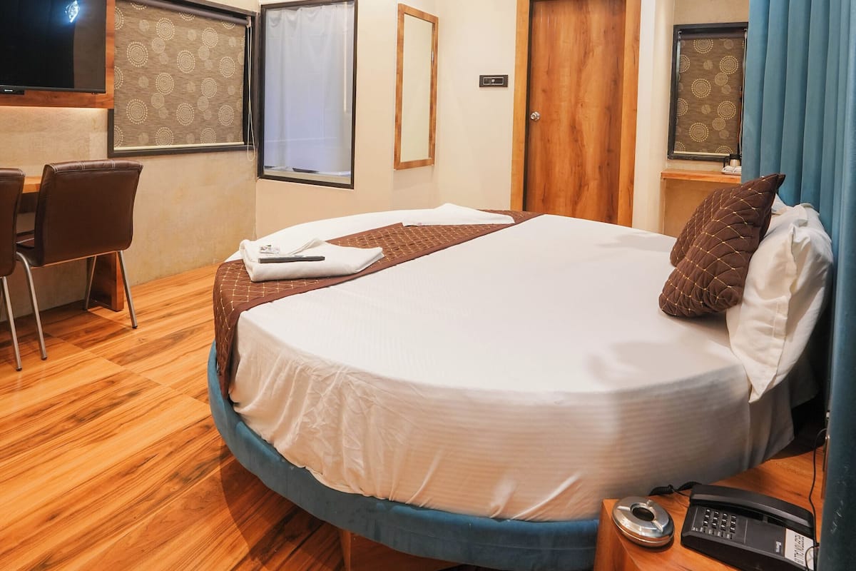 Moderni hotellihuone, jossa on pyöreä sänky, työpöytä, tuoli, kattotuuletin ja ilmastointilaite.